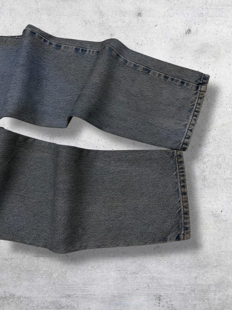 May include: Close-up of folded, dark gray denim jeans. The jeans have a classic five-pocket design with visible stitching and a faded appearance. The fabric appears to be a medium weight denim.