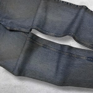 May include: Faded blue denim jeans, folded and laid flat. The jeans have a classic five-pocket design with visible stitching and a worn appearance. The fabric has a slightly textured look, suggesting a vintage or well-loved item.