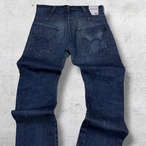 以下が含まれることがあります： 濃い色のデニムジーンズ。クラシックな5ポケットデザイン。ストレートレッグカットで、ボタンとジッパーで開閉します。バックポケットはユニークなカーブデザイン。バックウエストバンドに小さなタグが見えます。