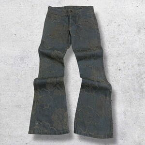 May include: A pair of blue denim jeans with a floral pattern. The jeans have a flared leg design and a button and zipper closure. The floral pattern is a lighter shade of blue and brown, creating a contrast against the darker denim.