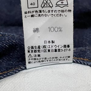 Puede incluir: Primer plano de una etiqueta blanca con texto y s&iacute;mbolos japoneses, probablemente una etiqueta de cuidado de la ropa. La etiqueta incluye instrucciones de lavado, contenido de la tela (100% algod&oacute;n) e informaci&oacute;n de fabricaci&oacute;n.