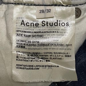 Op de afbeelding: Close-up van een wit label van Acne Studios jeans. Het label toont maat 29/32, de merknaam en de stijl "ACE RAW GOTHIC". Het geeft ook de materialen weer: 93% katoen, 6% polyester en 1% elastaan.