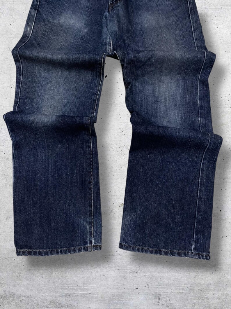 May include: Dark blue denim jeans with a classic five-pocket design. The jeans have a straight leg cut and show subtle fading and wear. The stitching is visible in a lighter thread color, and the fabric has a textured appearance.