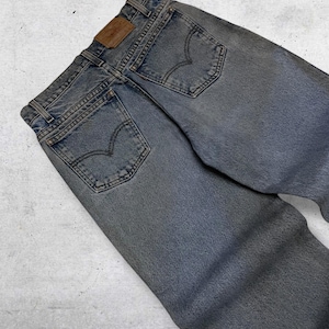 May include: Faded blue denim jeans with classic five-pocket styling. Features a brown leather patch and the iconic Levi's back pocket stitching. The jeans are pre-worn, showing signs of wear.