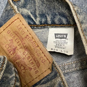 May include: Close-up of the inside of a pair of blue denim jeans. A brown leather tag with the Levi Strauss & Co. logo and text is visible, along with a white tag with the Levi's logo and size information: W29 L30.