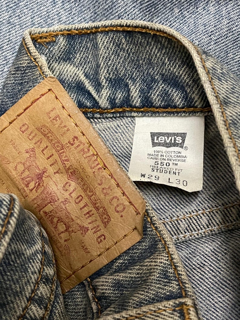 May include: Close-up of the inside of a pair of blue denim jeans. A brown leather tag with the Levi Strauss & Co. logo and text is visible, along with a white tag with the Levi's logo and size information: W29 L30.