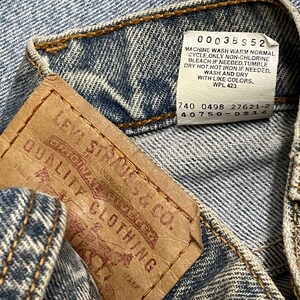 May include: Close-up of a denim garment with a brown leather tag and a white tag. The brown tag reads "LEVI STRAUSS & CO. QUALITY CLOTHING". The white tag has washing instructions. The denim is blue with visible stitching.