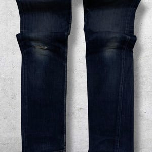 Op de afbeelding: Donkerblauwe denim jeans met een beschadigd kniedetail. De jeans hebben een klassiek vijf-zakken ontwerp en een rechte pijp. De denim heeft een vervaagde uitstraling, met subtiele kleurvariaties.