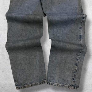 May include: Faded gray denim jeans. The jeans have a classic five-pocket design, with a straight leg cut. The denim has a worn appearance, with subtle fading and distressing throughout. The jeans are a versatile wardrobe staple.