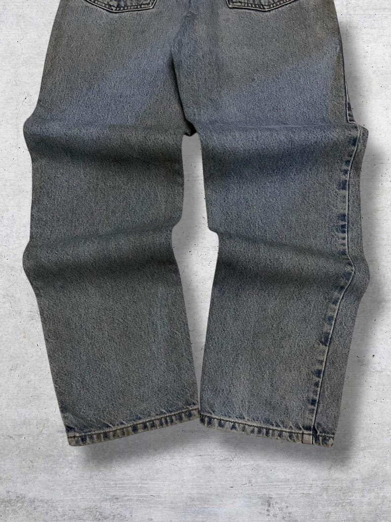May include: Faded gray denim jeans. The jeans have a classic five-pocket design, with a straight leg cut. The denim has a worn appearance, with subtle fading and distressing throughout. The jeans are a versatile wardrobe staple.