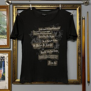 May include: Black short-sleeved t-shirt with a ribbed texture. The shirt features multiple lines of text in a distressed font. The text includes phrases like "You're Very The Highest" and "Dead or Alive Real Clothes."