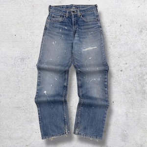 Puede incluir: Vaqueros de mezclilla azul claro con un aspecto desgastado. Los vaqueros tienen un lavado descolorido, una rodilla rasgada y salpicaduras de pintura blanca. Cuentan con un diseño clásico de cinco bolsillos y cierre de botón y cremallera.
