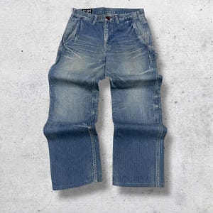 Könnte beinhalten: Hellblaue Jeans aus Denim mit verwaschener Optik und lockerer Passform. Die Jeans haben ein klassisches Fünf-Taschen-Design, einen Knopf- und Reißverschluss und ein kleines Etikett oben. Der Denim hat einen Used-Look.