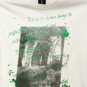 May include: Cream-coloured t-shirt featuring green handwritten text and a grayscale image. The text includes phrases like "It's up to human beings to protect the environment" and "people's hands."