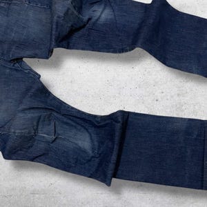 以下が含まれることがあります： 濃い青色のデニムジーンズが平らに置かれています。ジーンズは、クラシックな5ポケットのデザインとストレートレッグカットが特徴です。デニムは、わずかに色あせた外観で、微妙な色のバリエーションがあります。