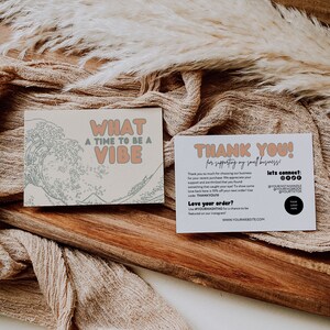 May include: A thank you card featuring a wave design and the text "What a time to be a vibe". The card is on a wooden surface with a beige fabric background. The text on the card says "Thank you for supporting my small business!" and includes a discount code "THANKYOU10".