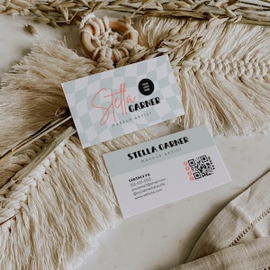 Könnte beinhalten: Zwei Visitenkarten mit einem blau-weiß karierten Hintergrund. Die obere Karte trägt den Text "Stella Garner Makeup Artist" und einen Platz für ein Logo. Die untere Karte trägt den Text "Stella Garner Makeup Artist" und Kontaktinformationen, darunter eine Telefonnummer, eine E-Mail-Adresse, einen Social-Media-Handle und eine Website. Ein QR-Code ist ebenfalls auf der unteren Karte enthalten.