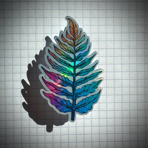 May include: A holographic fern leaf sticker with a rainbow gradient of pink, blue, and green.