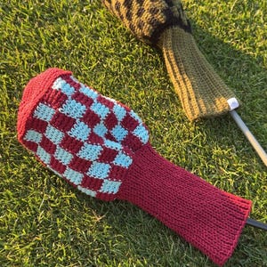 May include: Two crochet golf club head covers. One cover features a red and light blue checkered pattern with a solid red neck. The second cover displays a black and olive green diamond pattern with a solid olive green neck and a small white tag.