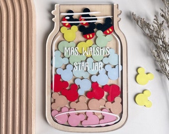 Könnte beinhalten: Ein Holztopf mit einer durchsichtigen Plastikfront, gefüllt mit bunten Mickey-Maus-Ohren. Der Topf trägt den Text "MRS. WALSH'S STAR JAR" auf der Vorderseite.