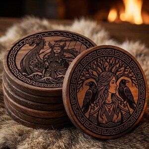 Pode incluir: Uma pilha de bases redondas de madeira com desenhos gravados intrincados. Uma base apresenta um navio viking e um guerreiro, enquanto outra retrata uma mulher com corvos e uma &aacute;rvore. As bases s&atilde;o castanhas escuras.