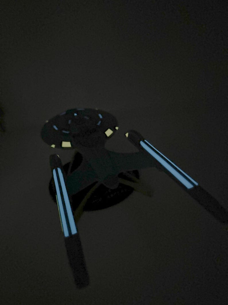 Puede incluir: Un modelo de nave espacial negro y azul con una parte superior circular y dos alas largas y delgadas. Las alas tienen una franja azul en el centro.