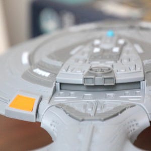 Puede incluir: Un modelo gris y naranja de una nave espacial con un dise&ntilde;o detallado. El modelo tiene una secci&oacute;n de puente elevada con una peque&ntilde;a luz azul.