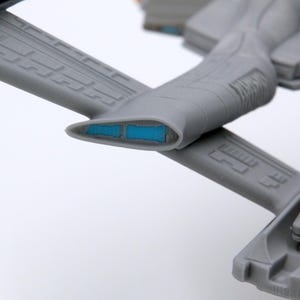 Puede incluir: Modelo gris detallado de una nave espacial, con paneles intrincados y detalles azules. El dise&ntilde;o incluye estructuras en forma de ala y un cuerpo central con un elemento azul brillante, lo que sugiere un tema futurista o de ciencia ficci&oacute;n.