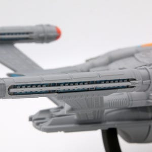 Puede incluir: Maqueta gris de una nave espacial con detalles en rojo y naranja. El modelo presenta componentes detallados del motor y alas. La nave se encuentra sobre un fondo blanco, mostrando sus intrincadas caracter&iacute;sticas.
