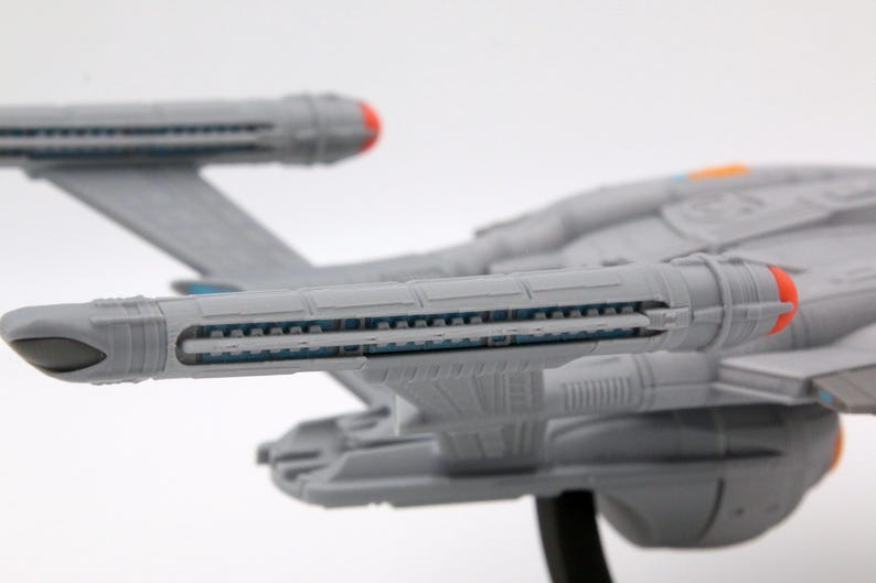 Puede incluir: Maqueta gris de una nave espacial con detalles en rojo y naranja. El modelo presenta componentes detallados del motor y alas. La nave se encuentra sobre un fondo blanco, mostrando sus intrincadas caracter&iacute;sticas.