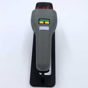 K&ouml;nnte beinhalten: Eine graue Star Trek Phaser-Replik mit einem schwarzen St&auml;nder. Der Phaser hat ein gr&uuml;n-gelbes Display und ein rotes Licht oben.