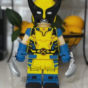 May include: A yellow and blue Wolverine action figure with a black mask and silver claws. The figure has a yellow torso with blue accents and a red and yellow emblem. The figure is a collectible item.
