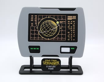 May include: A gray Star Trek Voyager PADD prop replica. The screen displays a sensor scan graphic with a grid and a globe. The PADD is mounted on a black stand.