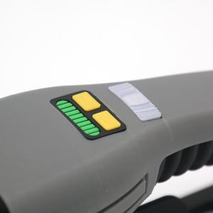 K&ouml;nnte beinhalten: Ein graues Handger&auml;t mit einem schwarzen Panel, auf dem sich ein gr&uuml;ner und gelber Knopf befindet. Das Ger&auml;t hat einen strukturierten schwarzen Griff.