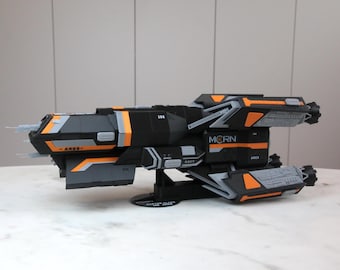May include: A black and orange spaceship model with the text "MCRN" on the side. The model is on a black base and has a detailed design.