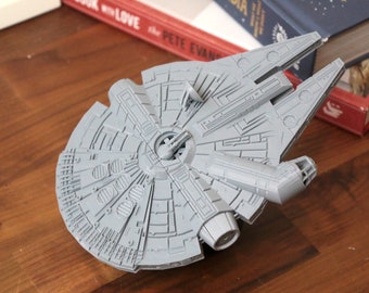 May include: A gray plastic model of the Millennium Falcon spaceship from Star Wars. The model is detailed with intricate lines and features.
