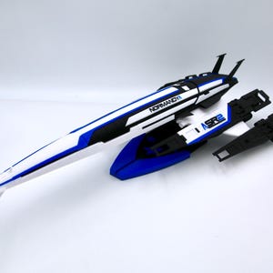 Puede incluir: Un modelo de nave espacial blanco y azul con detalles negros. El modelo está etiquetado como "NORMANDY" y "SR2".