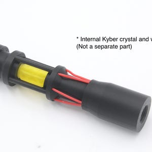 May include: A black cylindrical component featuring a yellow Kyber crystal encased within a cage-like structure, accented by thin red wires extending along the body. The text reads: * Internal Kyber crystal and wires (Not a separate part).