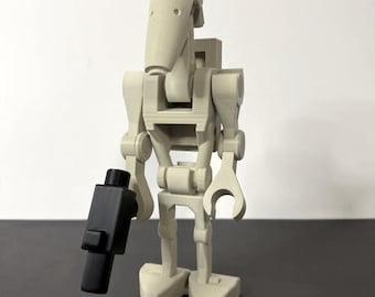 May include: A light tan battle droid figure with a black blaster. The droid has a distinctive elongated head and a segmented body. The figure is a collectible item, likely a replica or model.