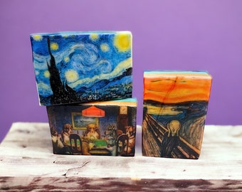 Puede incluir: Tres pequeñas cajas de madera con diferentes pinturas famosas impresas en ellas. La caja superior presenta una escena nocturna estrellada azul y amarilla, la caja del medio muestra un grupo de perros jugando a las cartas, y la caja inferior tiene una pintura de una persona gritando en un paisaje.