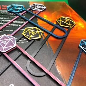 May include: Five 3D printed bookmarks shaped like dice with different colored accents. The bookmarks are attached to black metal clips. The dice are numbered 1, 20, 20, 1, and 20.