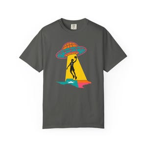 May include: Dark gray t-shirt featuring a basketball-themed graphic. The design includes a basketball-shaped UFO, a basketball player, and a colorful outline of a state. The UFO is orange and teal, with a pink outline. The player is black, and the state outline is blue, pink, and green.
