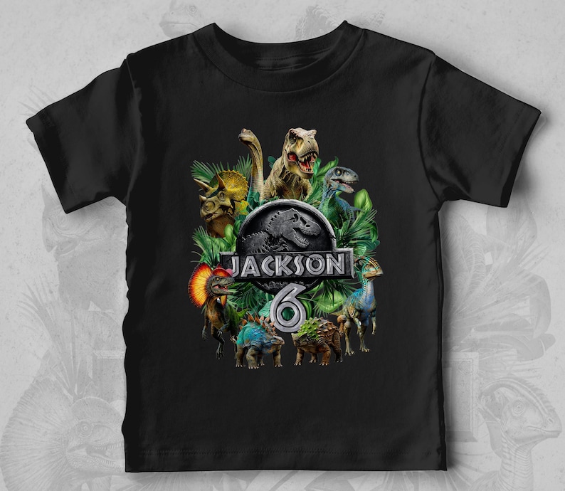 Peut inclure: T-shirt noir avec un motif de dinosaures et le texte "JACKSON 6". Le motif comprend divers dinosaures et le logo de Jurassic Park. Le t-shirt est fait d'une mati&egrave;re douce.