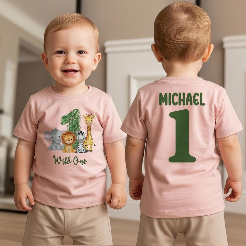 Pu&ograve; includere: T-shirt rosa a maniche corte con una grafica di animali della giungla e la scritta "Wild One". La parte anteriore della maglietta presenta un elefante, un leone, una zebra e una giraffa accanto al numero 1. Il retro della maglietta ha il nome "MICHAEL" e il numero 1.