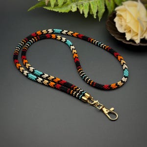 May include: A colorful beaded lanyard with a gold clasp. The lanyard is made of small, colorful beads in a geometric pattern.