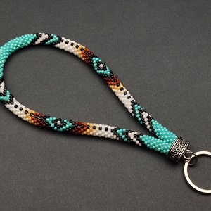 May include: A turquoise, white, black, and brown beaded keychain with a silver key ring.