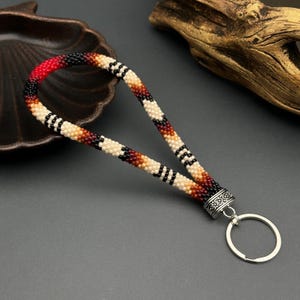 May include: A beaded key chain with a geometric pattern in red, black, white, and brown. The key chain has a silver metal ring and a silver metal clasp.