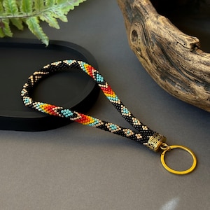 May include: A beaded lanyard with a black, turquoise, orange, and gold geometric pattern. The lanyard has a gold metal key ring attached.