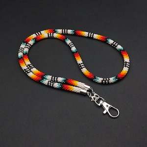 May include: A beaded lanyard with a colorful geometric pattern in red, orange, yellow, white, black, and blue. The lanyard has a silver clip.