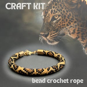 May include: Craft kit for a beaded crochet rope bracelet with a leopard print design. The bracelet is made with gold, black, and cream colored beads.
